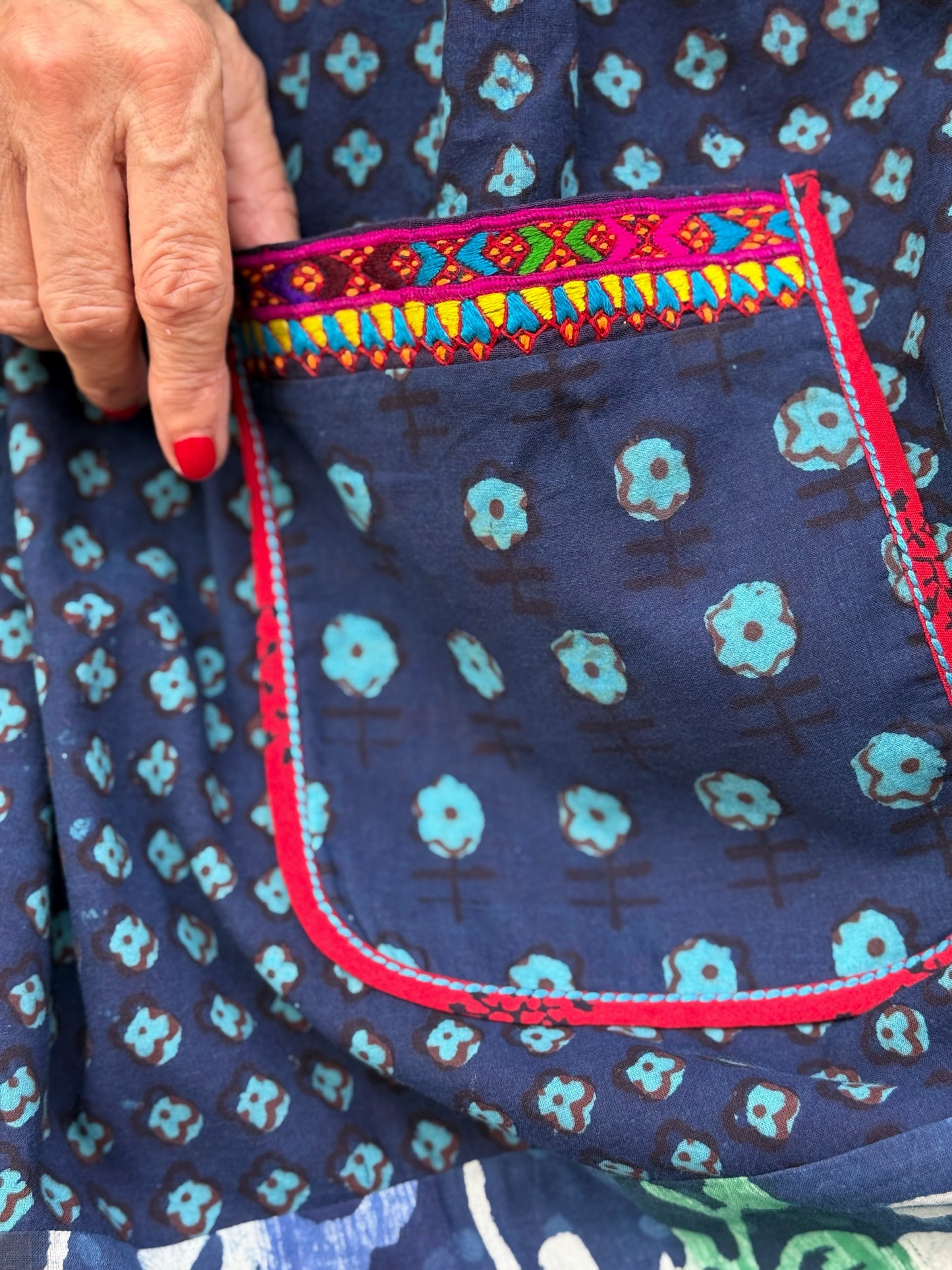 Button thru cotton dress in turquoise hues with red accents. All hand printed fabrics, this dress features vibrant Kutch hand embroidery.